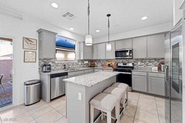 kitchen with sink, light tile patterned floors, appliances with stainless steel finishes, a center island, and light stone countertops