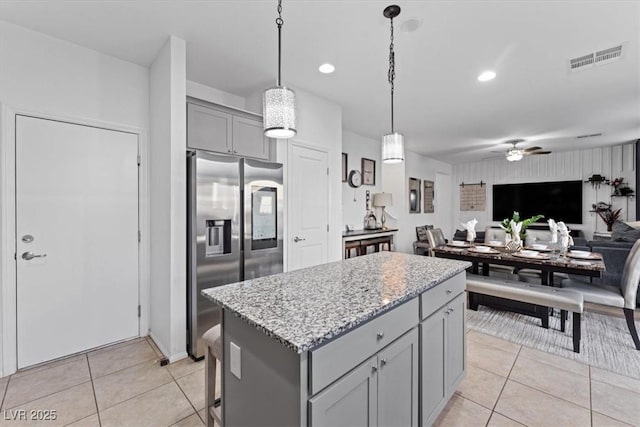 kitchen featuring pendant lighting, gray cabinetry, light stone counters, a kitchen island, and stainless steel fridge with ice dispenser