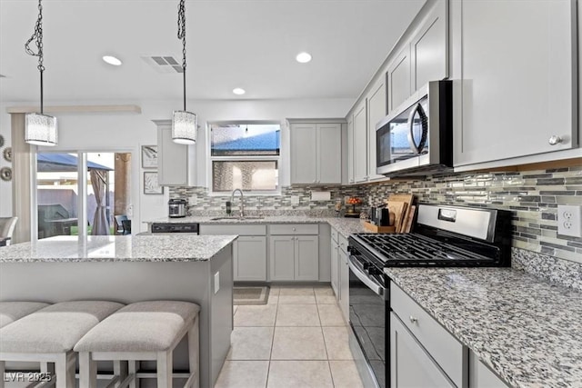 kitchen with sink, light stone counters, decorative light fixtures, appliances with stainless steel finishes, and a kitchen breakfast bar