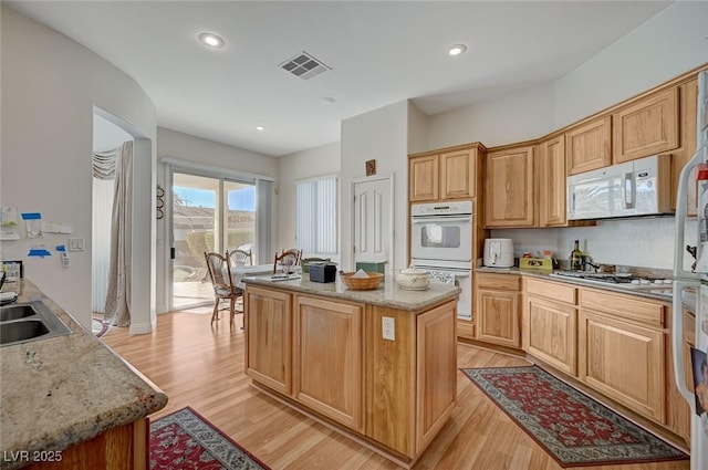 kitchen featuring sink, light wood-type flooring, a center island, light stone countertops, and white appliances