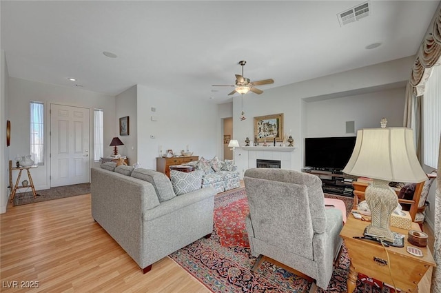 living room with ceiling fan, a fireplace, and light hardwood / wood-style floors