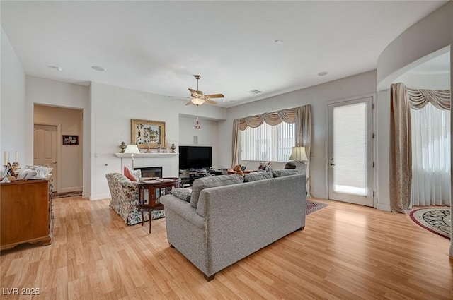 living room featuring a tile fireplace, ceiling fan, and light wood-type flooring