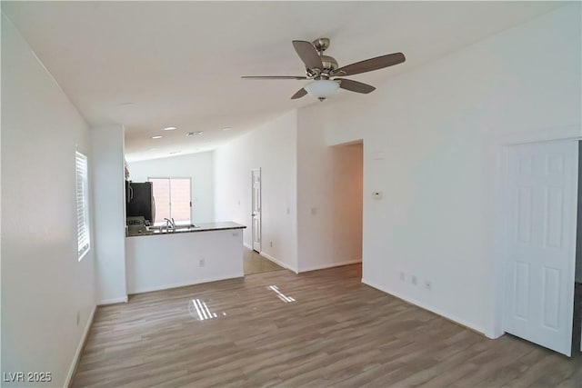 unfurnished living room with ceiling fan, lofted ceiling, sink, and light hardwood / wood-style floors