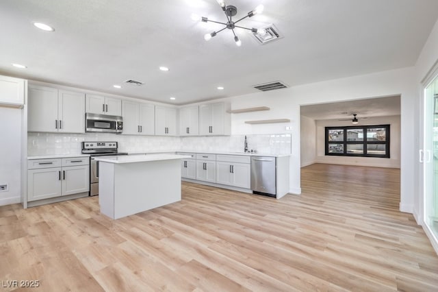 kitchen featuring sink, appliances with stainless steel finishes, white cabinetry, light hardwood / wood-style floors, and decorative backsplash