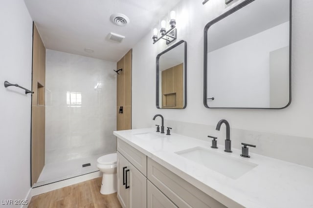 bathroom featuring hardwood / wood-style flooring, vanity, a tile shower, and toilet