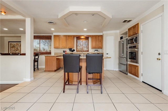 kitchen with a breakfast bar, a kitchen island, stainless steel appliances, light stone counters, and light tile patterned flooring