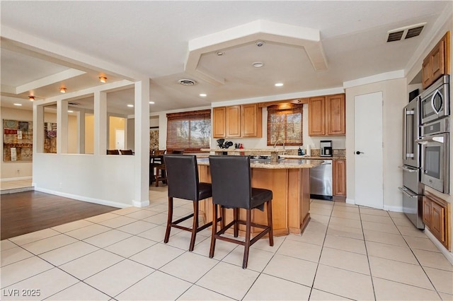 kitchen with light tile patterned flooring, a kitchen island, a breakfast bar area, stainless steel appliances, and light stone countertops