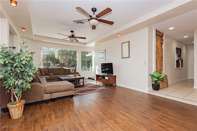 living room with light hardwood / wood-style floors, a raised ceiling, and ceiling fan