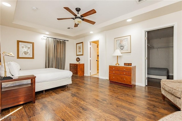 bedroom featuring dark hardwood / wood-style flooring, a walk in closet, a raised ceiling, and ceiling fan