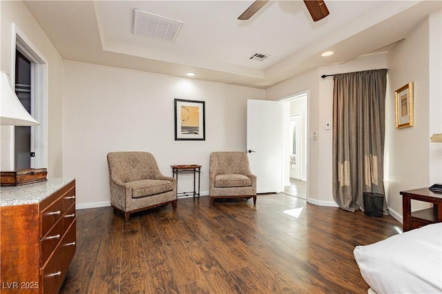 living area featuring a raised ceiling, dark hardwood / wood-style floors, and ceiling fan