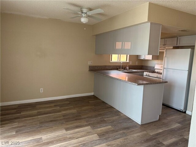 kitchen with dark hardwood / wood-style floors, white cabinetry, sink, kitchen peninsula, and white appliances