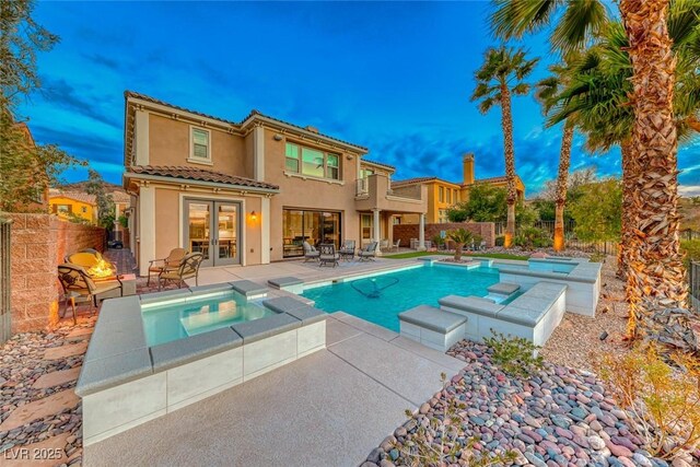 back house at dusk featuring a swimming pool with hot tub and a patio area