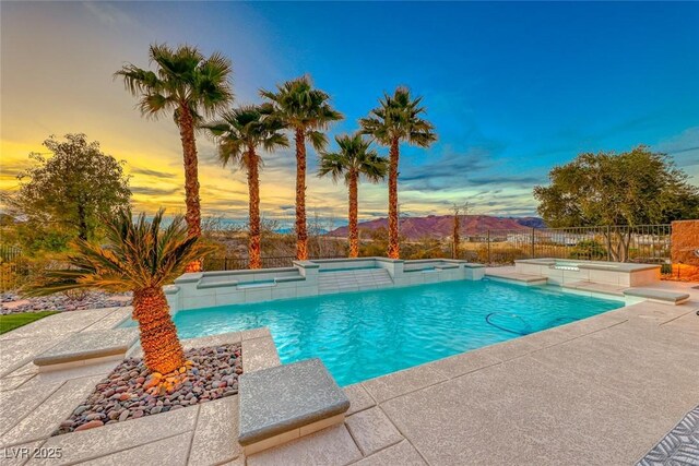 pool at dusk featuring a mountain view, a patio, and an in ground hot tub