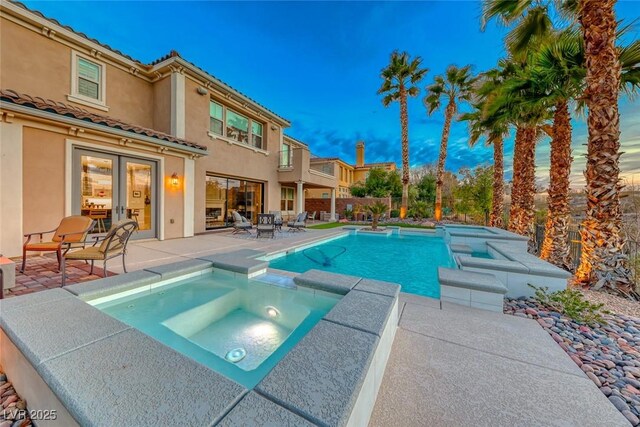 pool at dusk with an in ground hot tub and a patio area