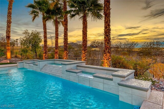 pool at dusk featuring an in ground hot tub and pool water feature