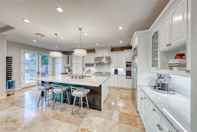 kitchen with a kitchen island with sink, pendant lighting, white cabinets, and light stone counters