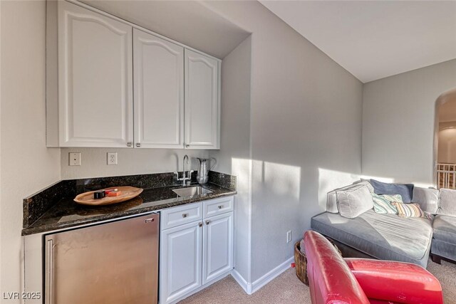 kitchen with sink, dark stone countertops, fridge, light colored carpet, and white cabinets