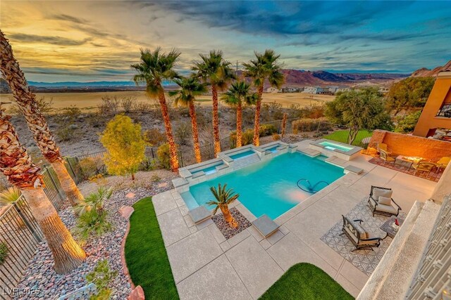 pool at dusk featuring an in ground hot tub and a patio