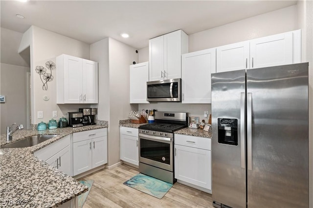 kitchen featuring sink, white cabinetry, stainless steel appliances, light stone counters, and light wood-type flooring