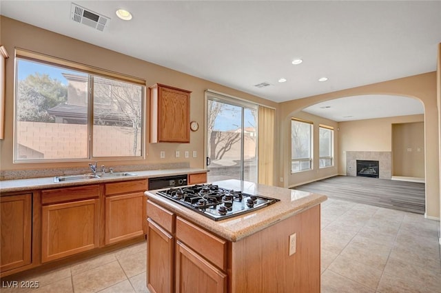 kitchen with light tile patterned flooring, stainless steel gas stovetop, black dishwasher, sink, and a center island