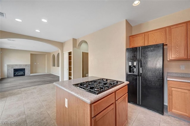 kitchen with a tiled fireplace, a kitchen island, light tile patterned floors, and black appliances