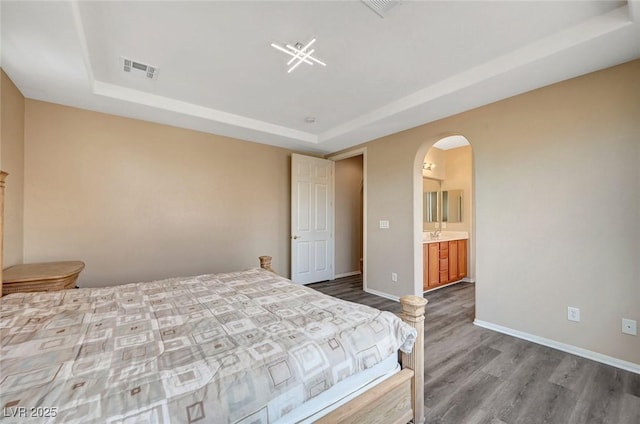 bedroom with ensuite bathroom, wood-type flooring, and a raised ceiling