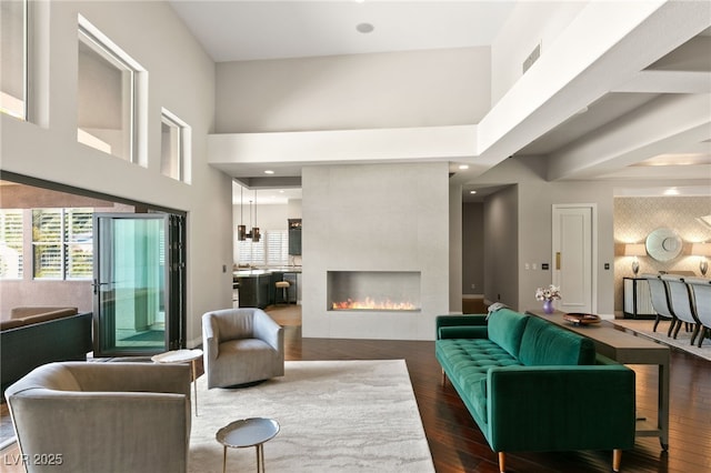 living room with a tiled fireplace, plenty of natural light, dark wood-type flooring, and a towering ceiling