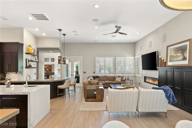 living room featuring french doors, ceiling fan, sink, and light hardwood / wood-style floors