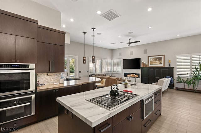 kitchen with stainless steel appliances, a center island, tasteful backsplash, dark brown cabinetry, and decorative light fixtures