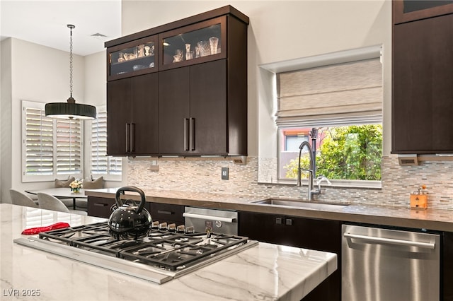 kitchen with pendant lighting, sink, stainless steel appliances, light stone countertops, and decorative backsplash