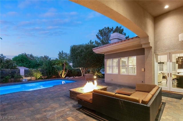 pool at dusk with a patio, an outdoor living space with a fire pit, and french doors