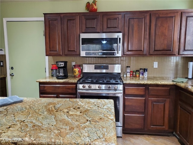 kitchen featuring light stone countertops, light wood-style flooring, stainless steel appliances, and backsplash