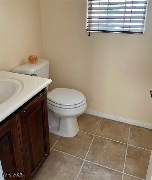 half bathroom featuring toilet, tile patterned floors, baseboards, and vanity