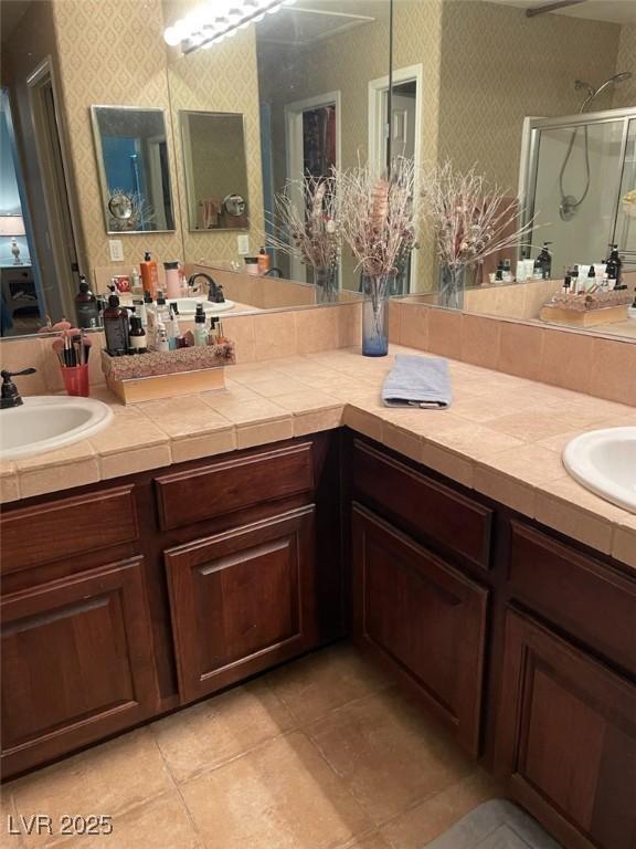 full bath with a stall shower, double vanity, a sink, and wallpapered walls