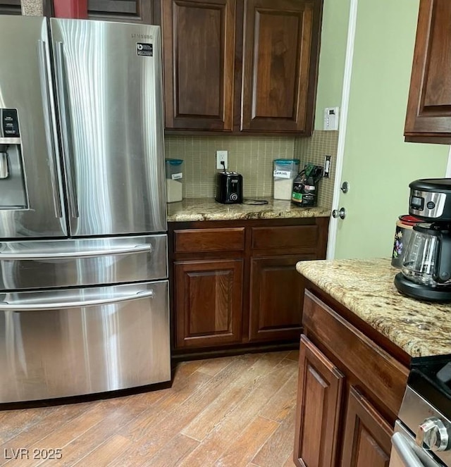 kitchen featuring light stone counters, stainless steel appliances, light wood-style flooring, decorative backsplash, and dark brown cabinets