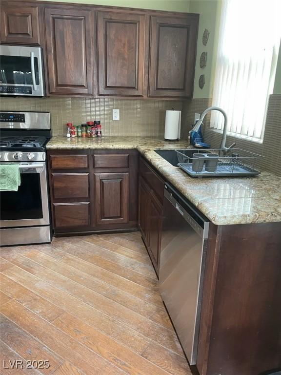 kitchen with a sink, dark brown cabinets, appliances with stainless steel finishes, decorative backsplash, and light wood finished floors