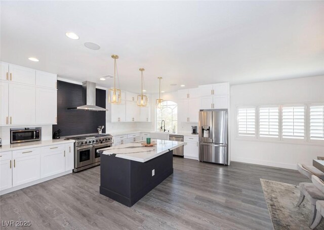 kitchen featuring a center island, hanging light fixtures, appliances with stainless steel finishes, wall chimney range hood, and white cabinets