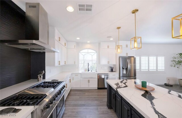 kitchen with pendant lighting, sink, appliances with stainless steel finishes, white cabinetry, and wall chimney exhaust hood