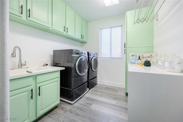 clothes washing area with cabinets, sink, washer and clothes dryer, and light wood-type flooring