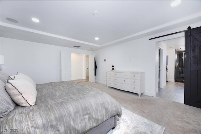 bedroom with a raised ceiling, a barn door, and light colored carpet