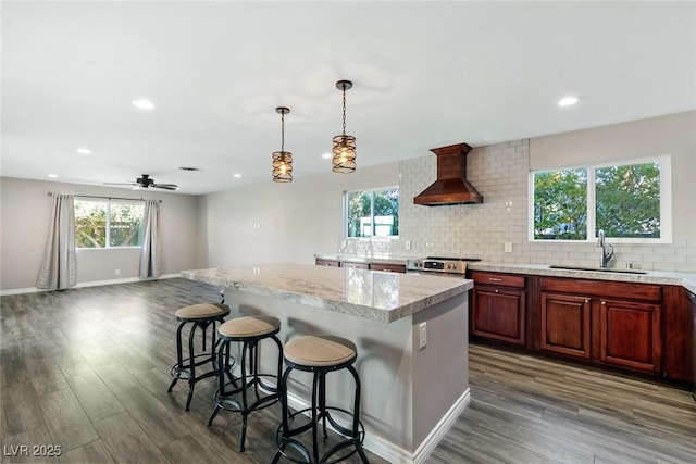 kitchen featuring premium range hood, a kitchen island, pendant lighting, sink, and a kitchen breakfast bar