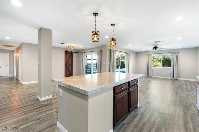 kitchen with pendant lighting, light hardwood / wood-style flooring, dark brown cabinets, a center island, and a barn door