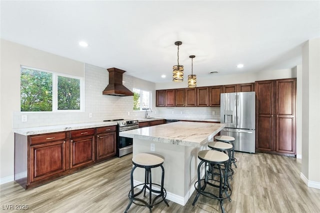 kitchen with sink, appliances with stainless steel finishes, custom range hood, a kitchen island, and decorative light fixtures