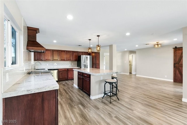 kitchen with decorative light fixtures, a kitchen island, stainless steel appliances, a barn door, and light stone countertops