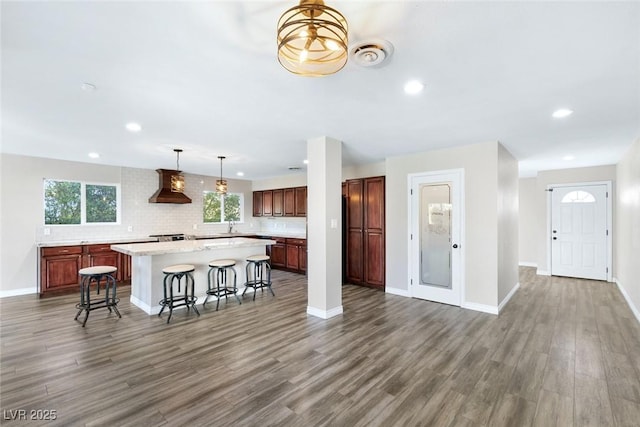 kitchen with dark hardwood / wood-style flooring, wall chimney range hood, a kitchen breakfast bar, and a center island