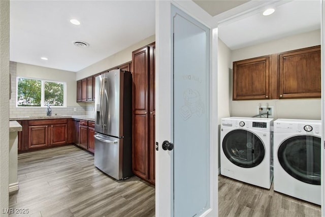 laundry room with cabinets, sink, washer and clothes dryer, and light hardwood / wood-style flooring