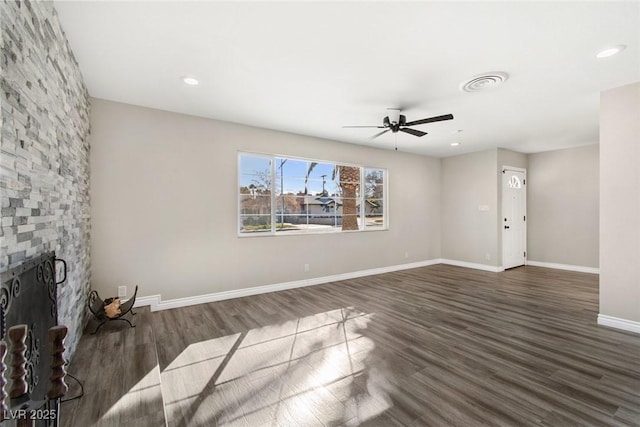 unfurnished living room featuring a stone fireplace, dark hardwood / wood-style floors, and ceiling fan