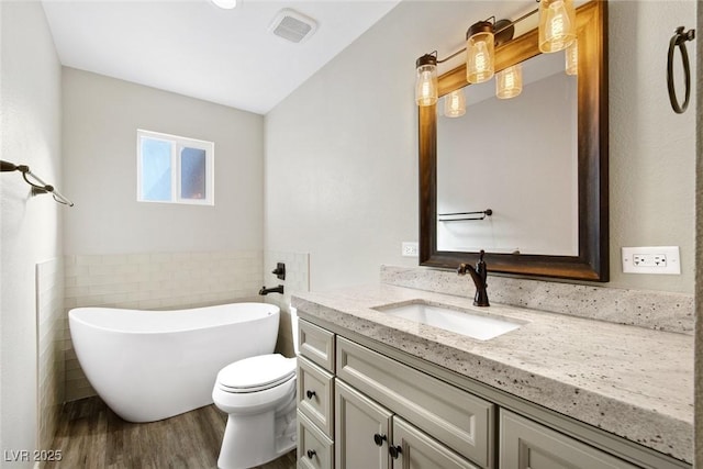 bathroom with hardwood / wood-style flooring, tile walls, vanity, a bath, and toilet