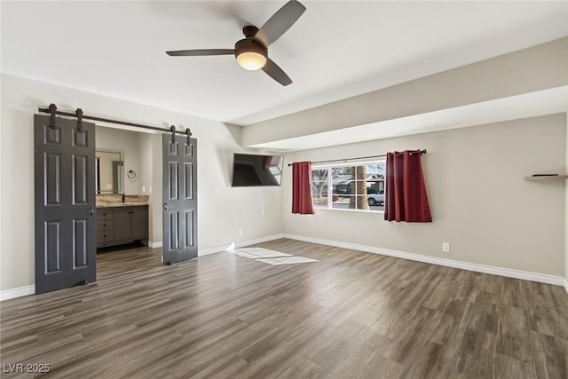 unfurnished bedroom featuring ceiling fan, a barn door, dark hardwood / wood-style floors, and ensuite bath