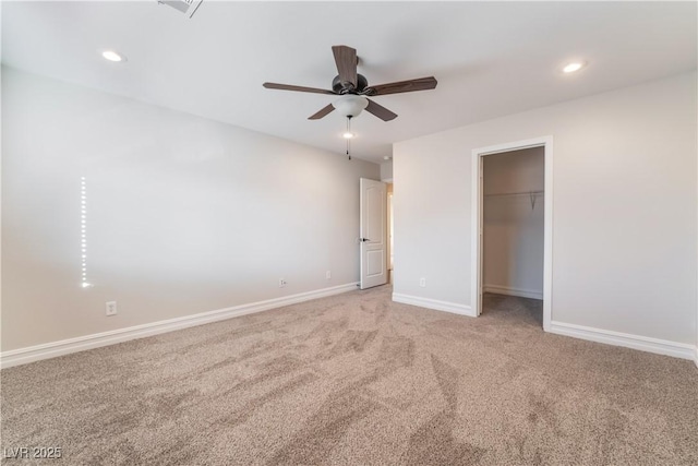 unfurnished bedroom with a walk in closet, a closet, ceiling fan, and carpet